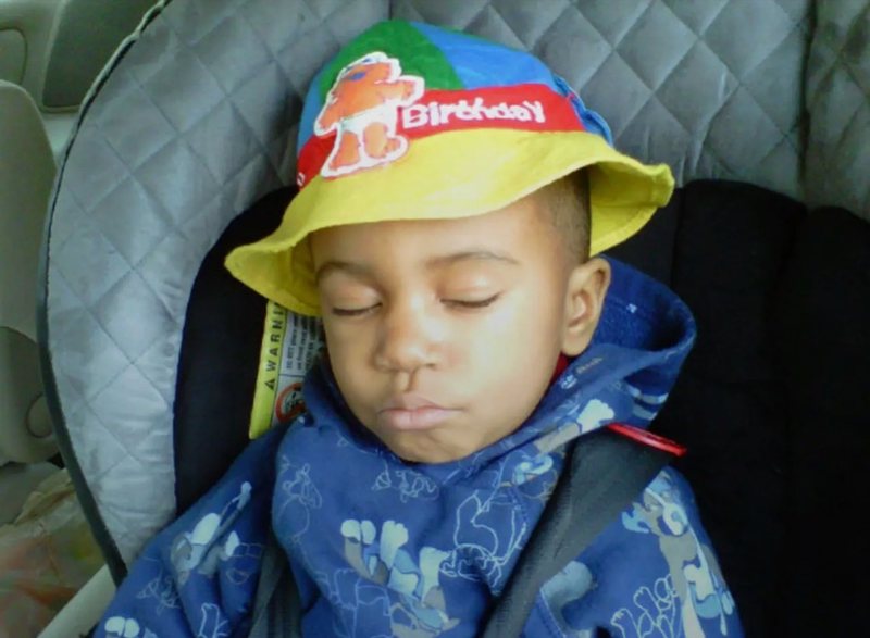 Theodore as a little kid asleep in a car seat, wearing a Birthday bucket hat