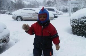 Theodore as a toddler in a red snowsuit and blue hat, standing in deep snow